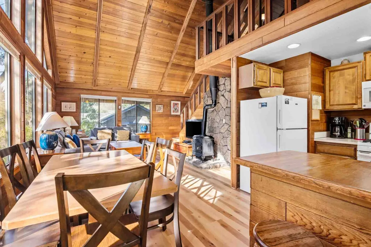 This image features a spacious living room with a cozy fireplace, a comfortable seating area, a large dining table, and expansive windows that let in natural light. The arrangement encourages communal gatherings and relaxation, with a warm, inviting mood ideal for adults and family conversations.