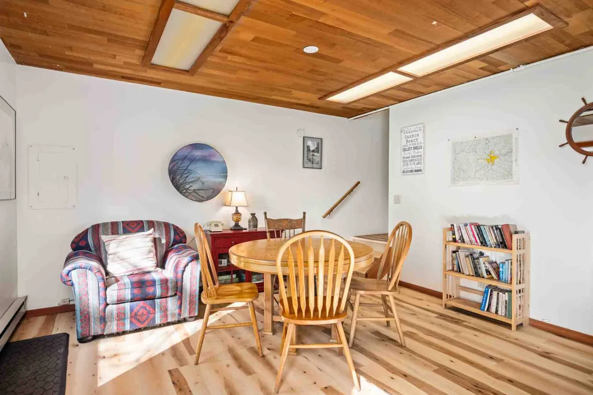 A cozy space featuring a striped armchair, a wooden dining table ideal for family meals, a bookshelf, and a lamp. The setup invites guests to sit with a cup of coffee, enjoy a meal, or dive into a good book while basking in a tranquil, home-like setting.