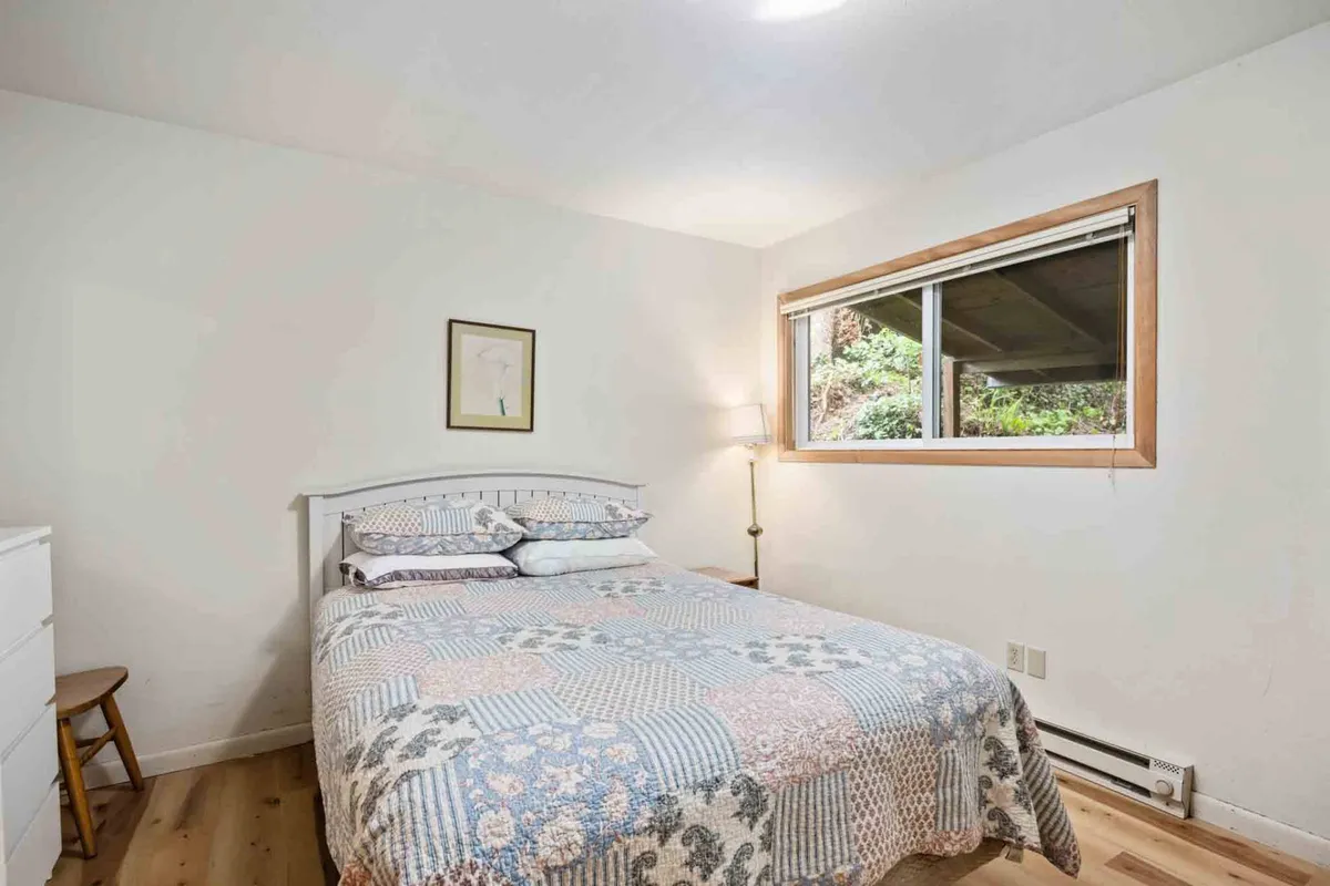 A cozy bedroom with a bed dressed in a patterned quilt, a lamp beside the bed, and a window bathing the space in soft, natural light. The atmosphere feels serene and welcoming, ideal for relaxation.