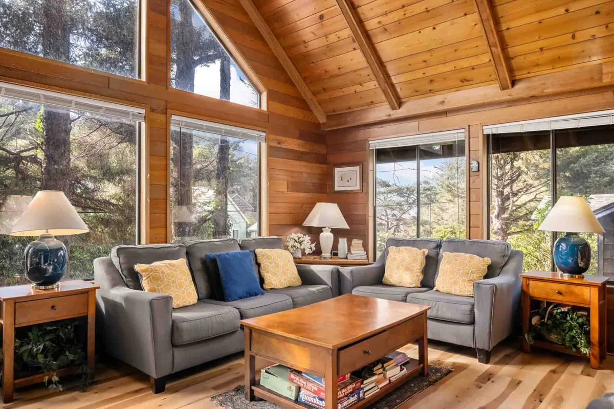 A bright and inviting living room with comfortable sofas and a wooden coffee table, framed by large windows that allow plenty of natural light to pour in. Decorative lamps and tasteful decor create a warm, communal atmosphere, ideal for both relaxation and socializing.