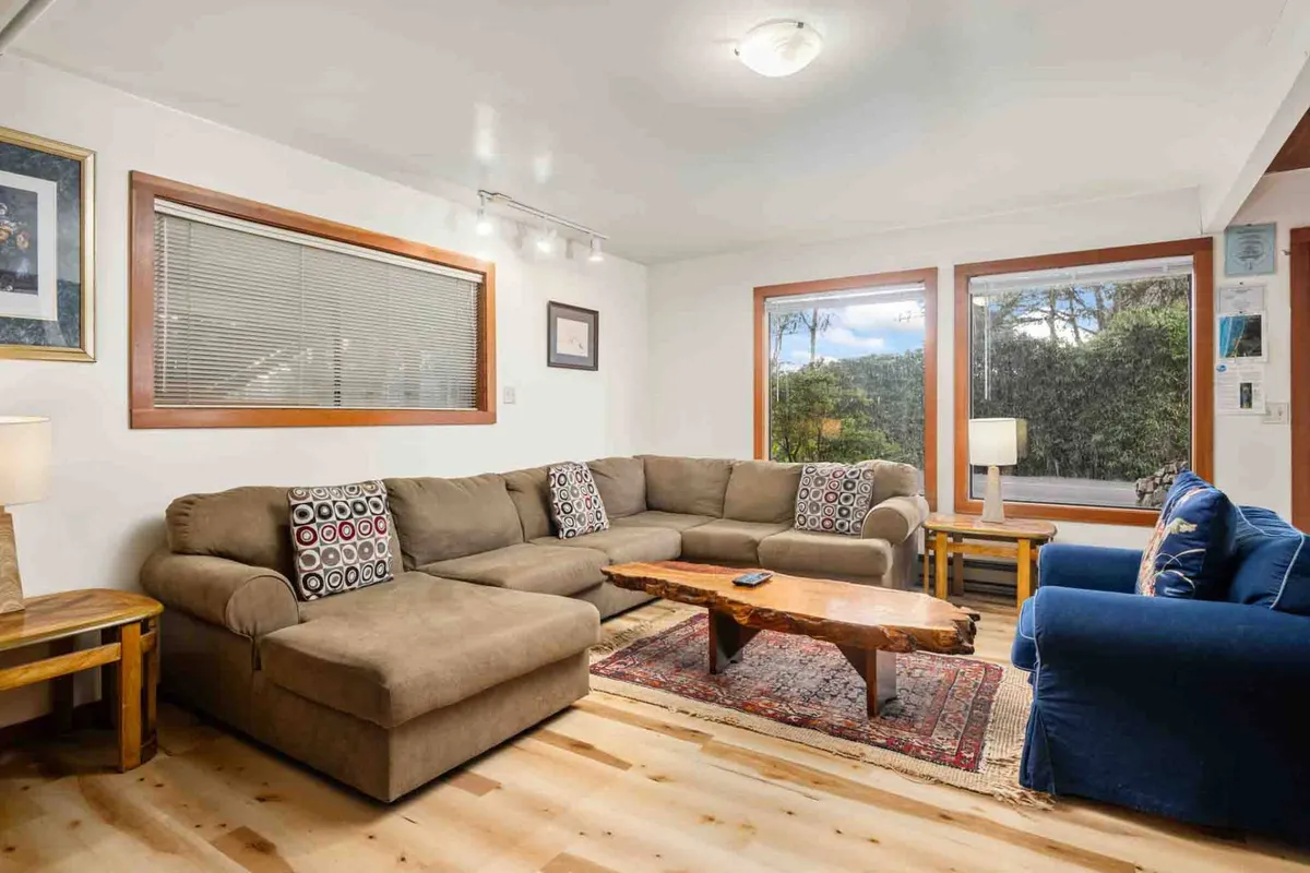 This image showcases a welcoming lounge space with a large sectional sofa, a live edge coffee table, curated artwork, and broad windows offering scenic views. The room exudes comfort and encourages socializing, reading, or unwinding in a serene setting.