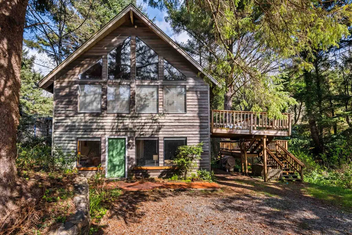 A welcoming exterior shot of the home featuring large windows, a green front door, and a spacious wooden deck surrounded by lush greenery. The setting radiates tranquility and hints at the leafy, shaded environment ideal for both pets and their owners.