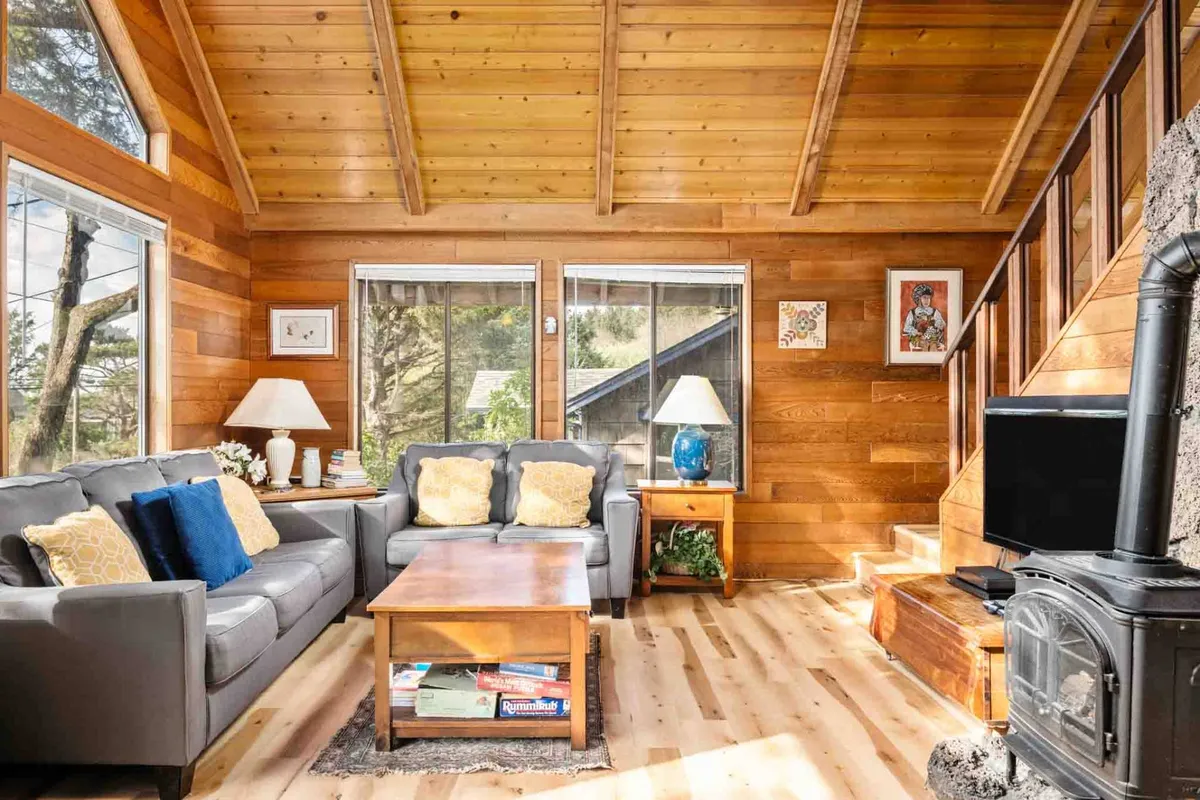 A welcoming living area showcasing a sofa with yellow pillows, a wooden coffee table, and a fireplace. Large windows brighten the space, reinforcing a sense of warmth and comfort, while the fireplace suggests cozy evenings spent together.