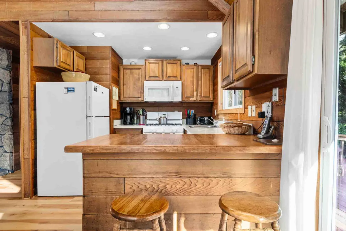A warm, welcoming kitchen featuring wooden cabinetry, a central island with bar stools, and modern kitchen appliances. The space is set up for both cooking and social interaction, ideal for family breakfasts or festive group meal preparations.